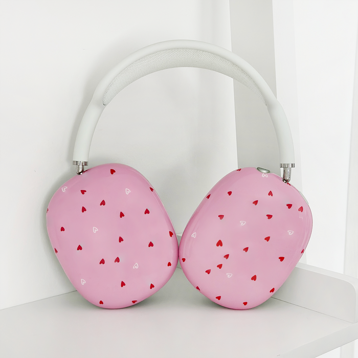 Pink AirPods Max case with red and white hearts pattern on a white shelf.