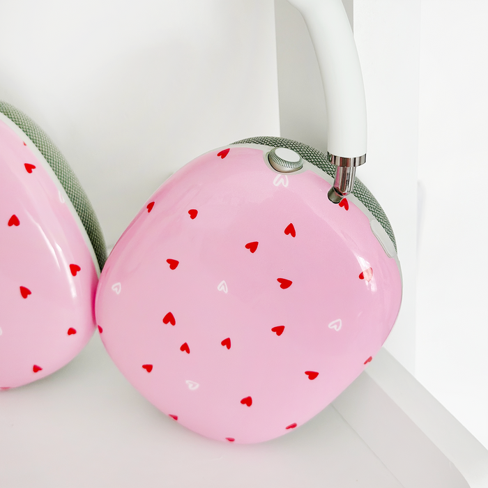 Pink AirPods Max case with red and white heart pattern, shown on a white surface.