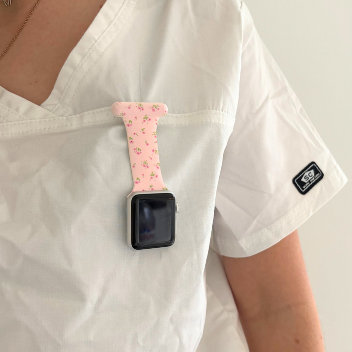 Pink ditsy floral Apple Watch clip-on fob strap attached upside down to a white scrub top pocket.