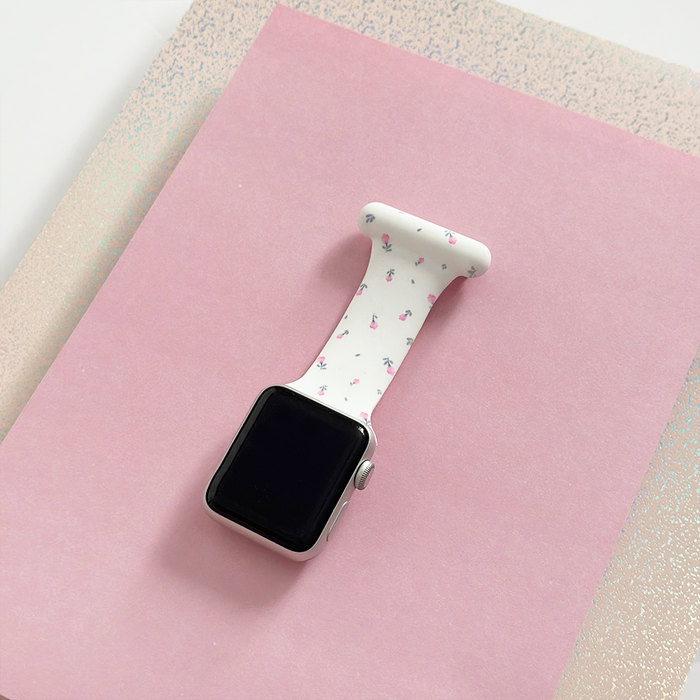 Coconut Lane Apple Watch clip-on fob strap in white with ditsy floral print, displayed on pink paper and glittery beige background.