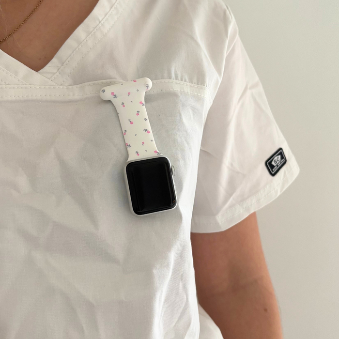 Coconut Lane Apple Watch clip-on fob strap in ditsy floral white attached to the chest pocket of a white scrub top.