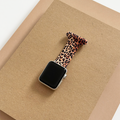 Leopard print Apple Watch clip-on fob strap by Coconut Lane displayed on a brown textured card against a tan background.