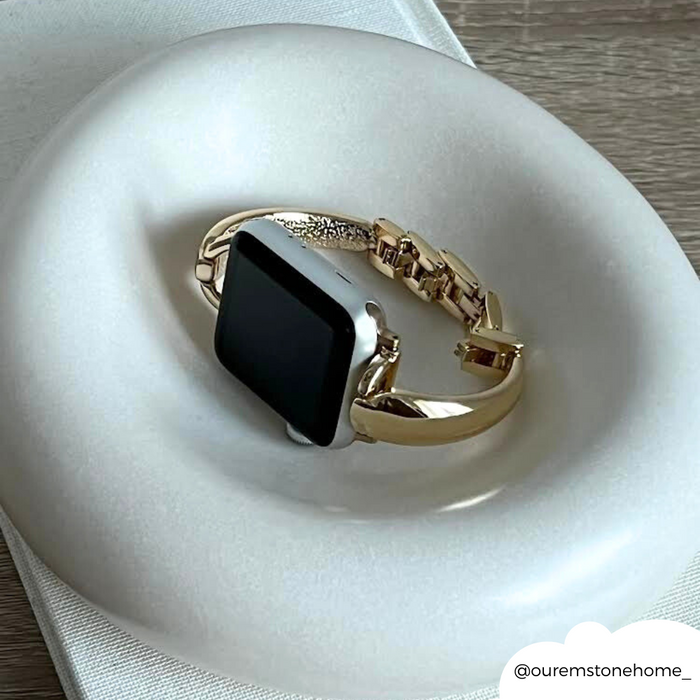 Gold Coconut Lane bangle-style Apple Watch strap on a round white dish with a matching gold smart watch.