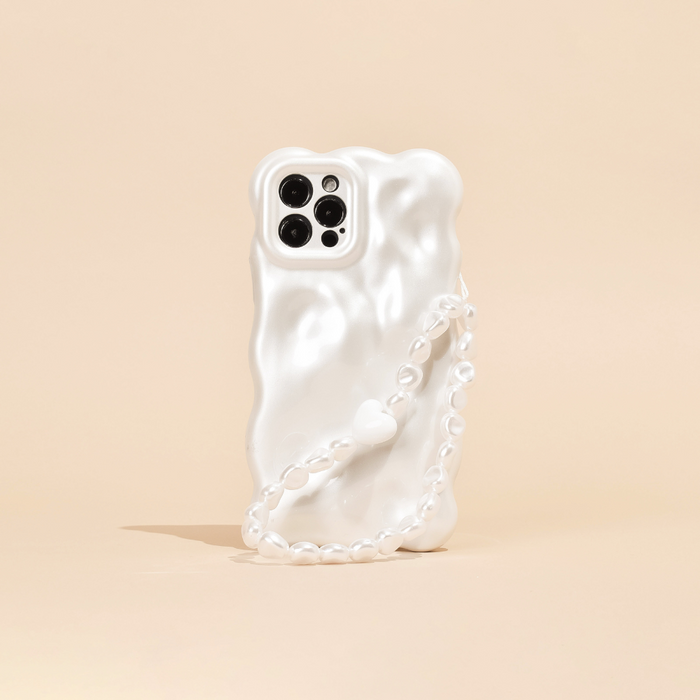 A white, wavy-textured phone case is shown standing on a light beige surface, featuring Coconut Lane's Beaded Phone Strap - Chunky Pearls. The phone's camera section with multiple lenses is visible, contributing to a sleek and modern aesthetic.