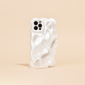 A white, wavy-textured phone case is shown standing on a light beige surface, featuring Coconut Lane's Beaded Phone Strap - Chunky Pearls. The phone's camera section with multiple lenses is visible, contributing to a sleek and modern aesthetic.