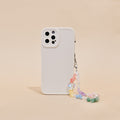 Beaded phone strap with colourful crystals attached to a white phone case on a beige surface.