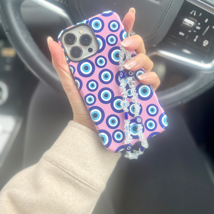 Hand holding a phone with a Coconut Lane beaded Crystal Evil Eye case and strap, shown inside a car.
