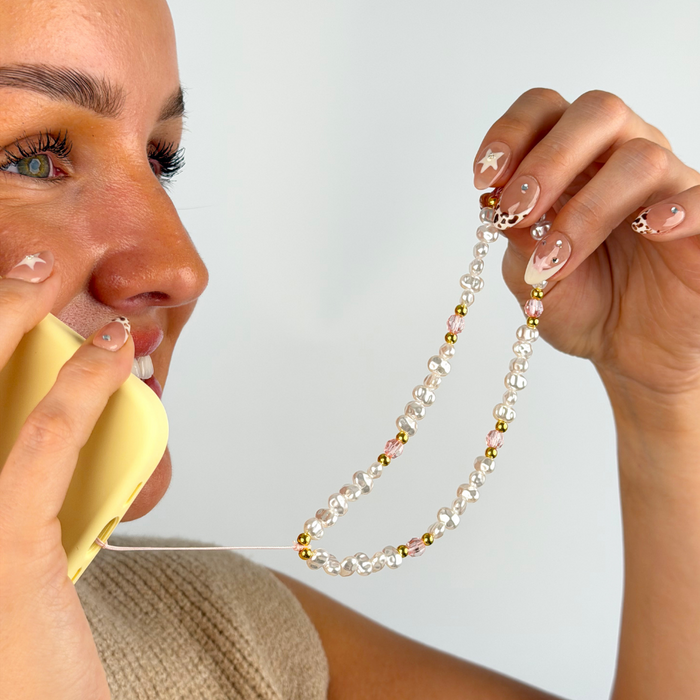 girl smiling on the phone with her pink gold and pink phone strap attached