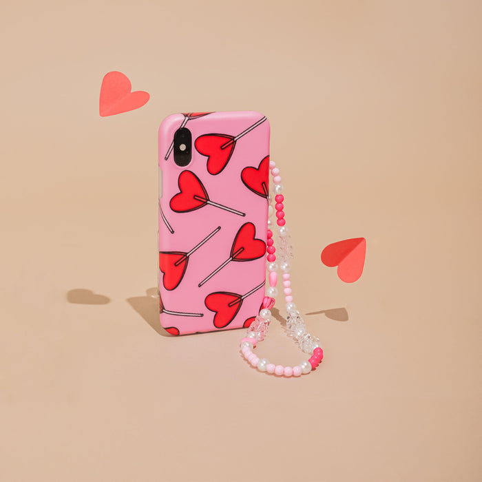 Pink beaded phone strap with red heart accents, shown on a beige background with scattered paper hearts.