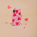 Pink beaded phone strap with red heart accents, shown on a beige background with scattered paper hearts.