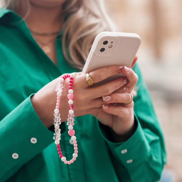Person in green shirt holding a white phone with a pink beaded Coconut Lane phone strap, typing with both hands.