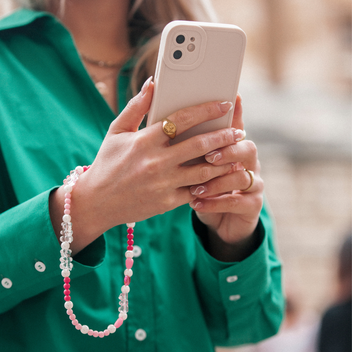 Woman in green shirt holding smartphone with pink beaded Coconut Lane phone strap attached.