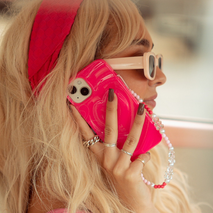 Woman with long blonde hair holds a phone with a pink beaded strap, wearing a matching pink headband.
