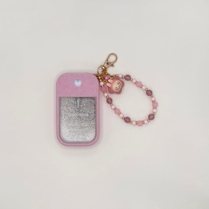 Touchland Power Mist hand sanitizer in a soft pink silicone case with a glitter window on a white background. Attached gold lobster clasp keychain features a small white Labubu chibi charm in a flower frame, paired with a beaded wrist strap of pink, mauve, clear, and gold accent beads with a green speckled bead detail. TOUCHLAND NOT INCLUDED WITH THIS PRODUCT!