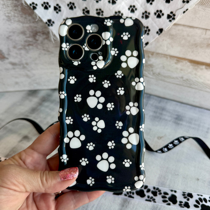 Black wavy iPhone case featuring a pattern of white paw prints held in hand, showing glossy finish.