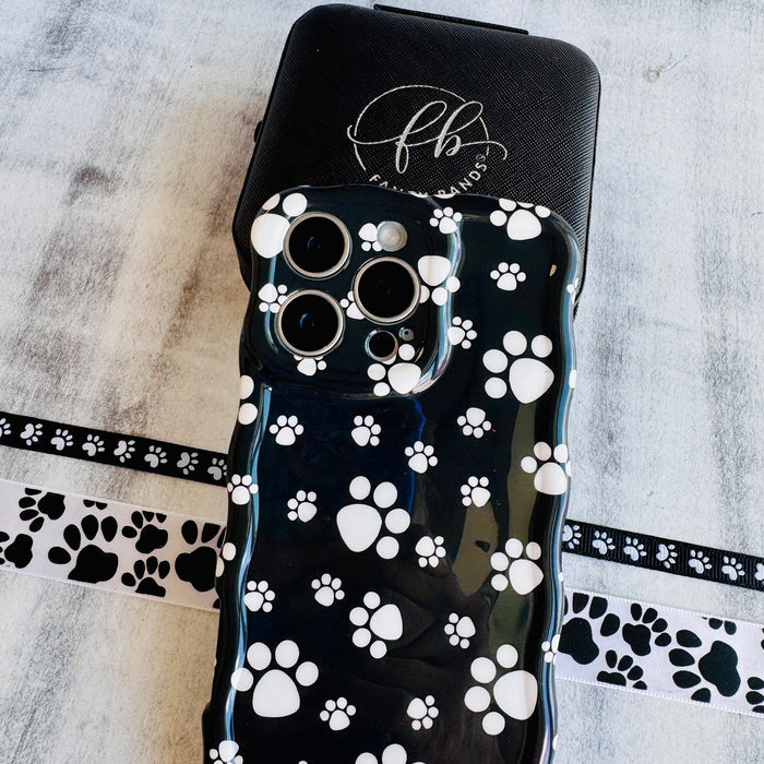 Black wavy iPhone case featuring a pattern of white paw prints held in hand, showing glossy finish.
