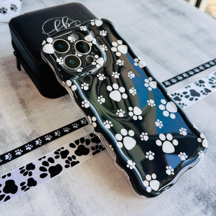 Black wavy iPhone case featuring a pattern of white paw prints held in hand, showing glossy finish.