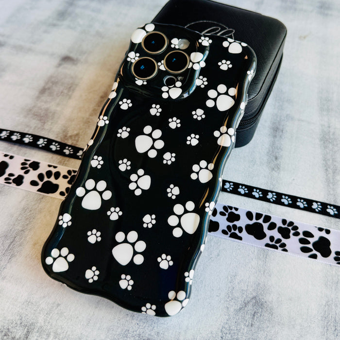 Black wavy iPhone case featuring a pattern of white paw prints held in hand, showing glossy finish.