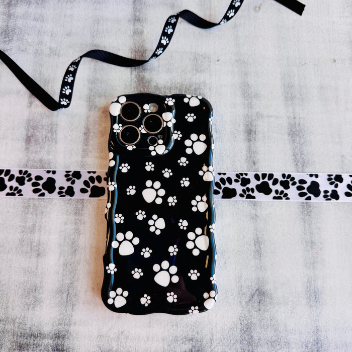 Black wavy iPhone case featuring a pattern of white paw prints held in hand, showing glossy finish.
