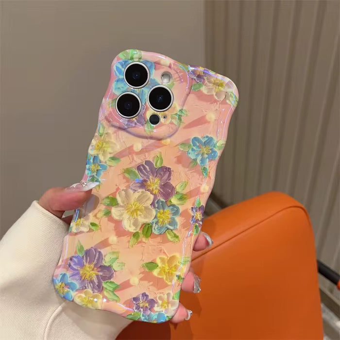 Soft pink wavy iPhone case featuring painterly flowers in purple, blue, and yellow with a glossy finish.