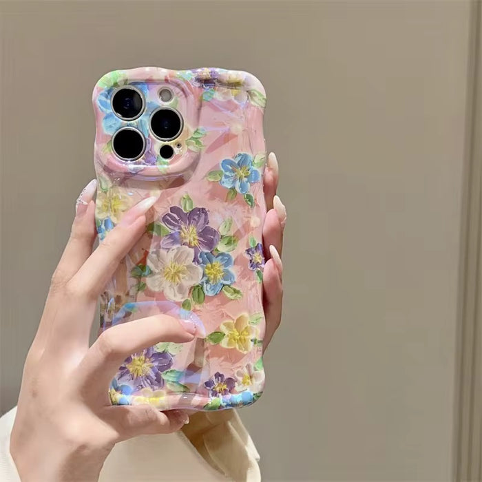 Soft pink wavy iPhone case featuring painterly flowers in purple, blue, and yellow with a glossy finish.