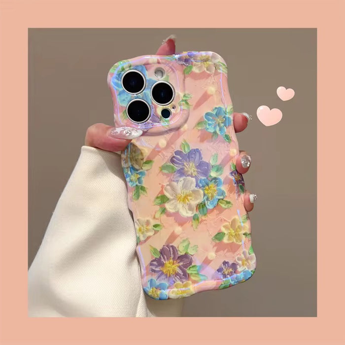Soft pink wavy iPhone case featuring painterly flowers in purple, blue, and yellow with a glossy finish.