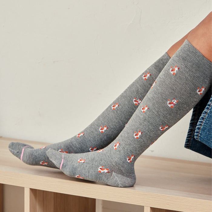 Knee-high gray compression socks with a cat pattern and pink accents, displayed on a wooden surface.