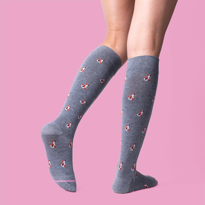 Knee-high gray compression socks with a cat pattern, shown on a model against a pink background.