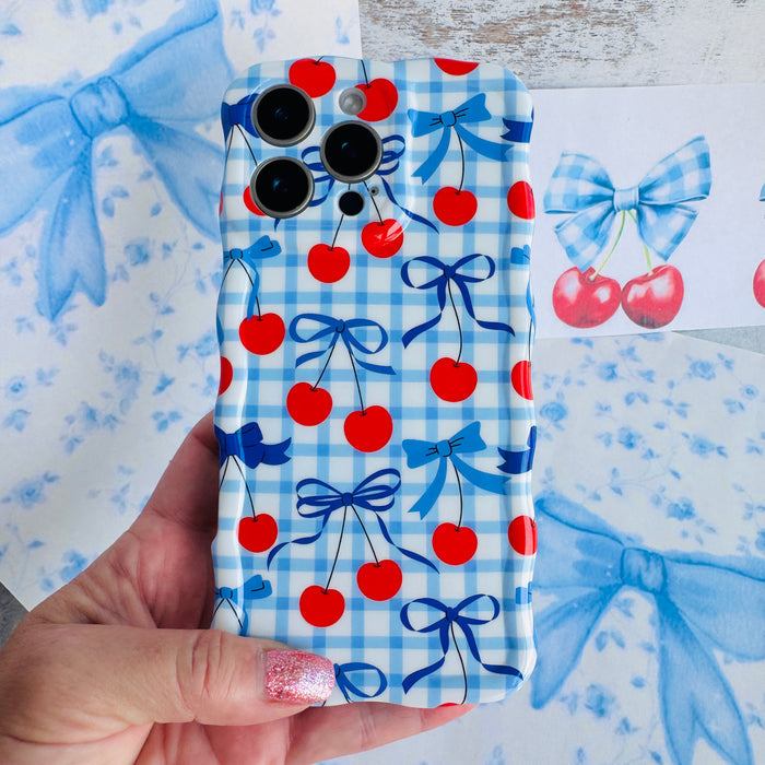 Blue and white gingham iPhone case featuring red cherries and blue ribbon bows with wavy edges.