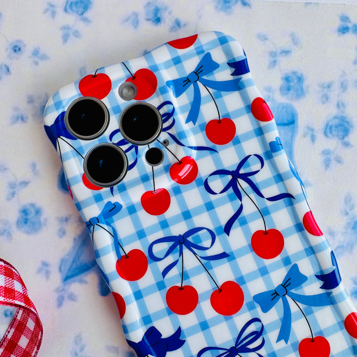 Blue and white gingham iPhone case featuring red cherries and blue ribbon bows with wavy edges.
