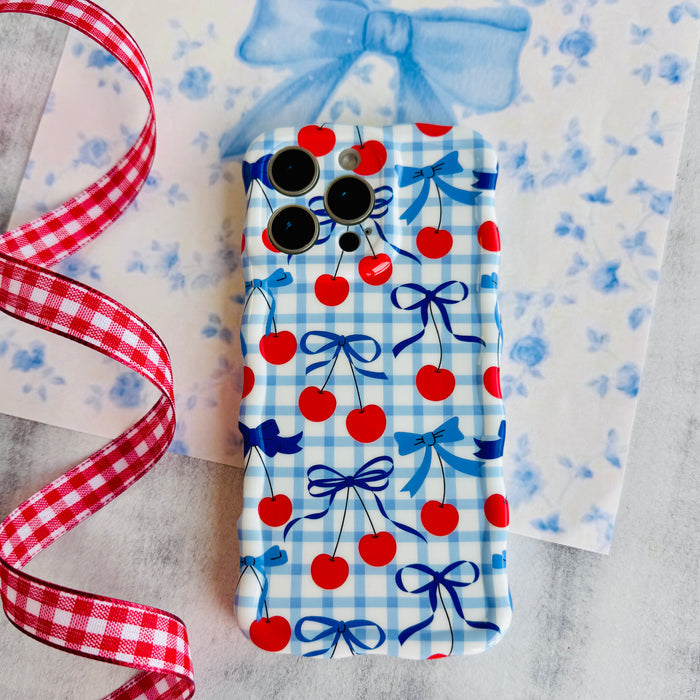 Blue and white gingham iPhone case featuring red cherries and blue ribbon bows with wavy edges.