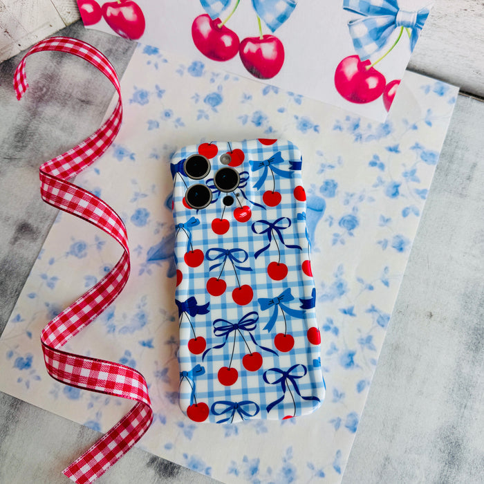 Blue and white gingham iPhone case featuring red cherries and blue ribbon bows with wavy edges.