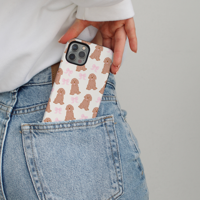 A hand slips a Coconut Lane Bows & Besties phone case with dog and bow print into blue jeans pocket.