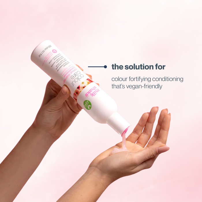 Hand holding a bottle of 'milk_shake' hair product with pink liquid being applied to palm on a light pink background.