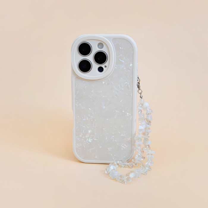 White iPhone with a pearlescent case and Coconut Lane Moonstone crystal phone strap on a light peach background.