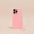 A pink smartphone case featuring Coconut Lane's Crystal Phone Strap - Rose Quartz is displayed on a beige background. The case features precise cutouts for three camera lenses and a flash. The pink beaded strap, adorned with genuine rose quartz crystals, is attached to the side of the case, providing an elegant decorative touch.