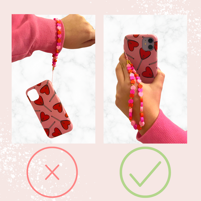 Two hands hold a red heart-shaped phone case with Coconut Lane’s colorful crystal beaded phone strap attached.