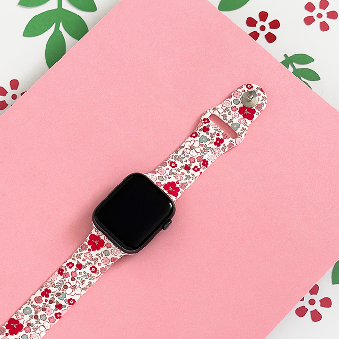 Coconut Lane floral Apple Watch strap on a pink surface, featuring green and red flower patterns in the background.