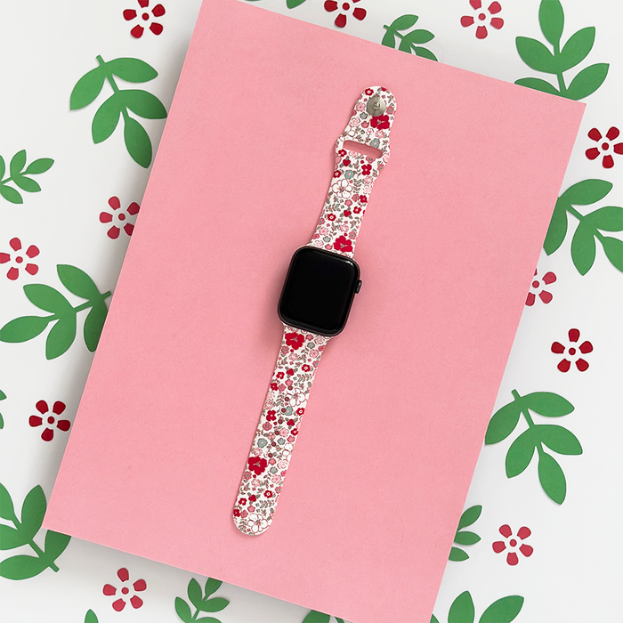 Apple Watch strap with floral pattern, displayed on a pink background with leaves and flower details.
