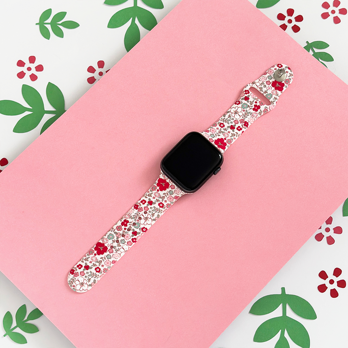 Pink Apple Watch strap with red and white flowers, green leaves, and floral accents by Coconut Lane.