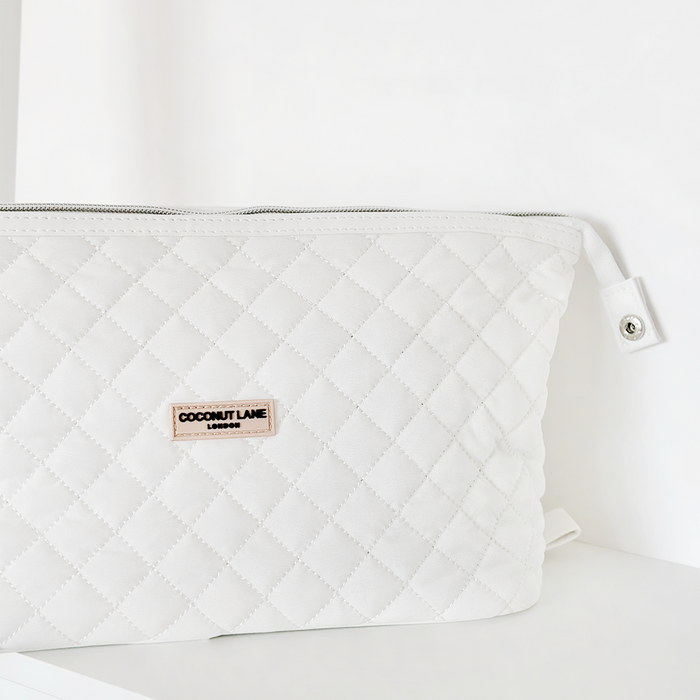White quilted expandable makeup bag with front label and zipper.