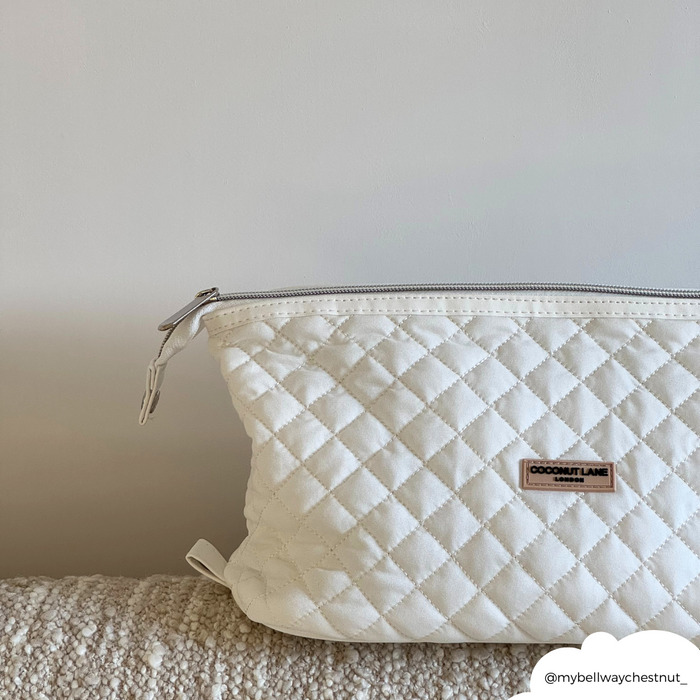Quilted milky white expandable makeup bag from Coconut Lane on a textured beige surface with a plain background.