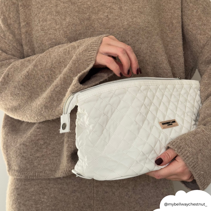 A person in a beige sweater holds a quilted white Coconut Lane expandable makeup bag with a gold logo.