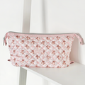 Pink quilted makeup bag with teddy bear pattern, displayed on a white shelf.