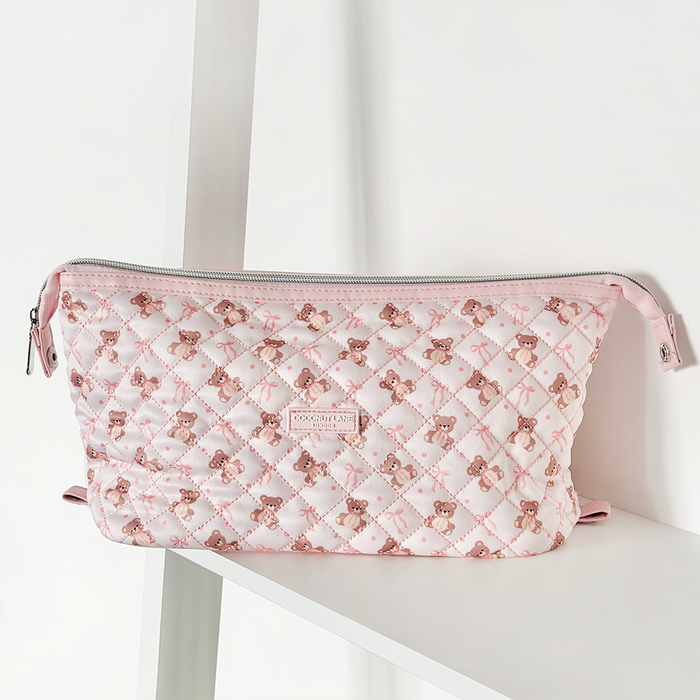 Pink quilted makeup bag with teddy bear pattern, displayed on a white shelf.