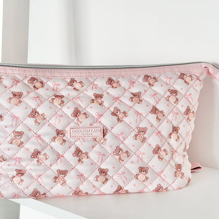 Pink quilted Coconut Lane Expandable Makeup Bag with teddy bear and ribbon print, displayed on a white shelf.