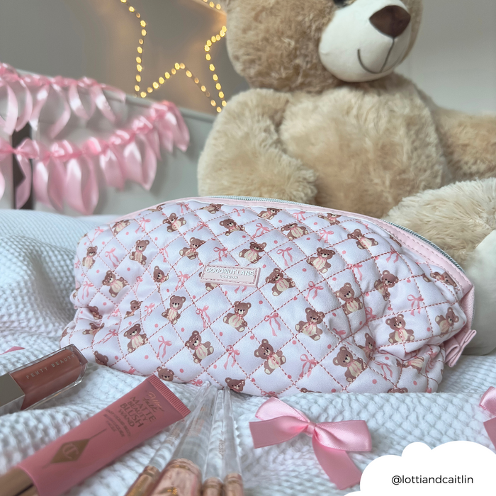 Pink quilted Coconut Lane expandable makeup bag beside makeup items and a plush teddy bear.