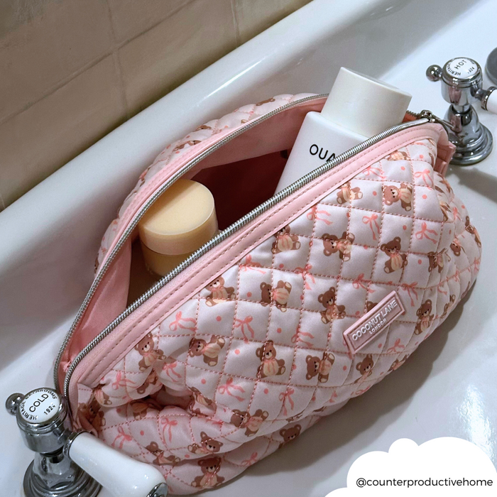 Pink quilted Coconut Lane makeup bag unzipped in a sink, holding assorted bottles and containers.