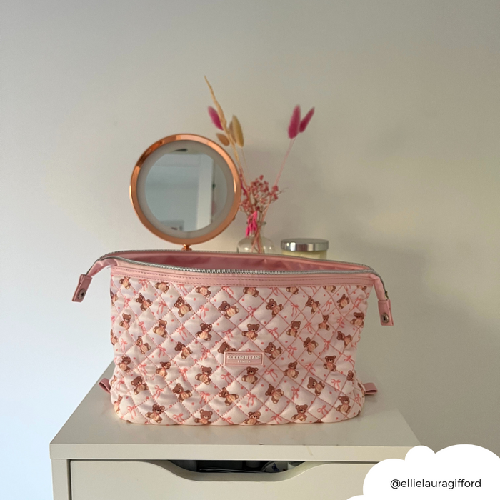 Quilted beige Coconut Lane Expandable Makeup Bag on a white dresser beside a round mirror and dried flowers.