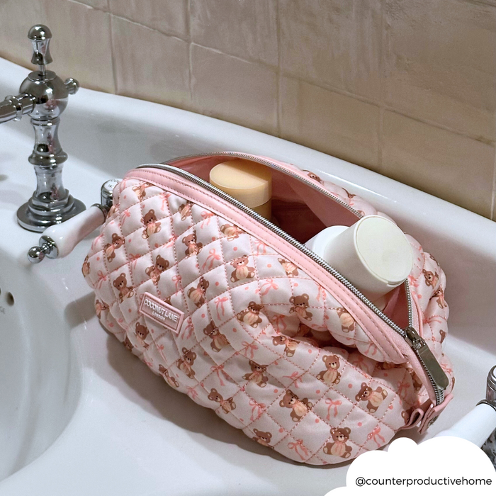 Pink quilted Coconut Lane Teddy makeup bag open on a sink, with bottles visible inside.